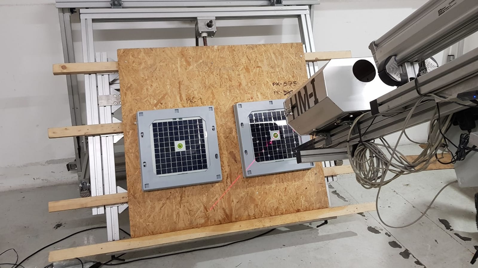 Two Tessera HAIL sensors mounted on a target board at the IBS Hail Lab, with the ice launcher's barrel aimed at one and a red alignment laser across its solar panel