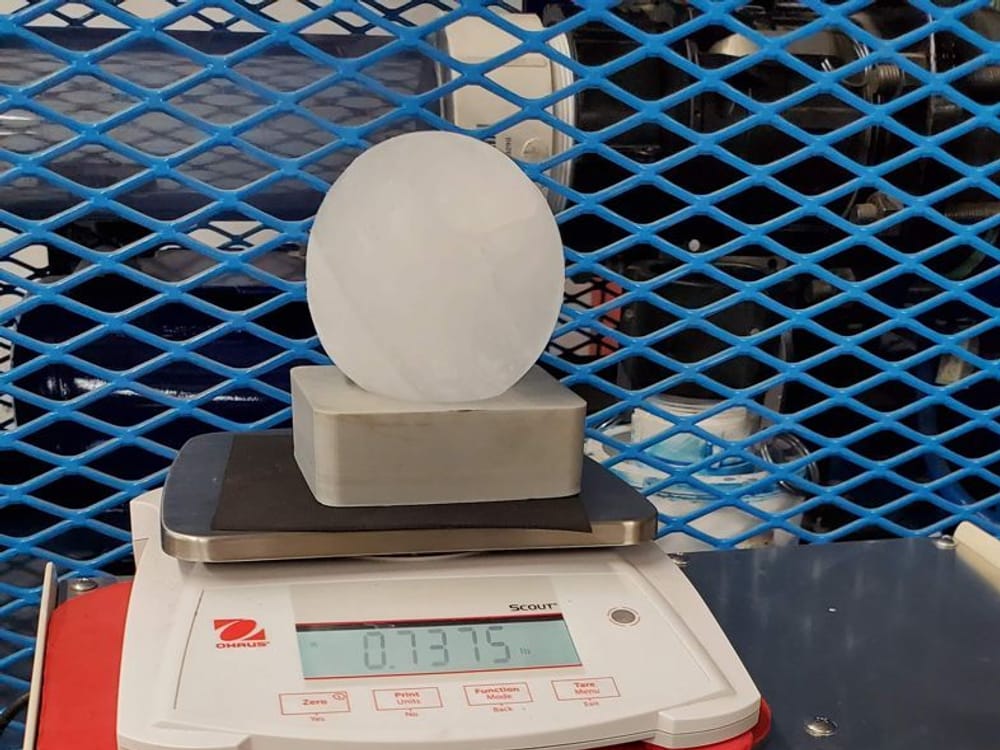A laboratory ice sphere resting on a digital scale at Koontz Labs, its mass shown on the display