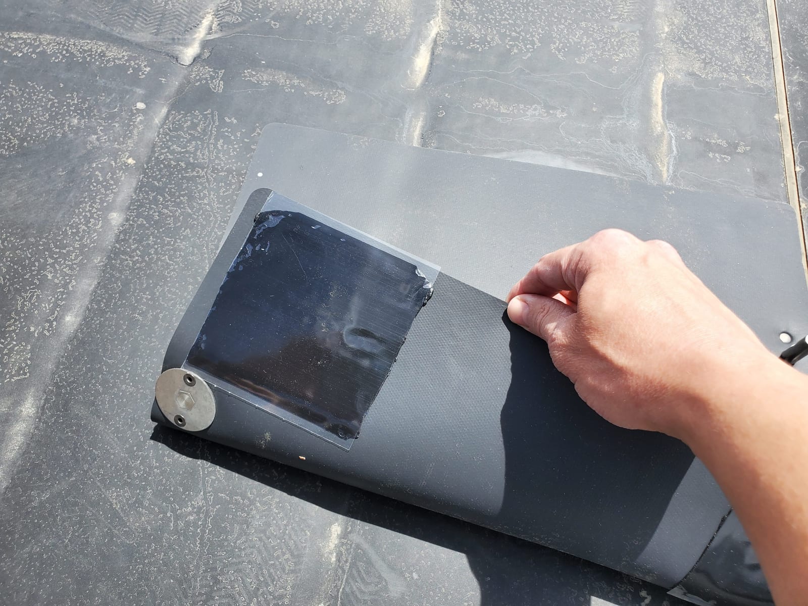 An installer's hand pressing an adhesive mounting pad and bracket onto a flat roof membrane