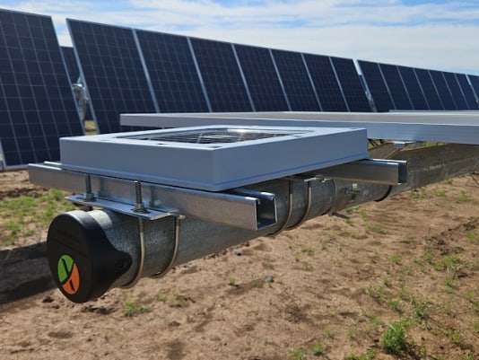 A Tessera sensor mounted on the torque tube of a utility-scale solar tracker, rows of photovoltaic panels behind it under a blue sky
